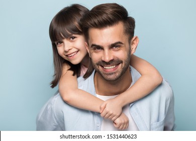 Close up portrait of happy preschool girl piggyback hug young father posing together isolated on blue studio background, smiling little daughter embrace father look at camera, family picture concept - Powered by Shutterstock