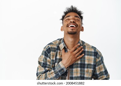 Close Up Portrait Of Happy, Relieved And Carefree African American Guy 20s Years, Laughing Out Loud, Raise Head Up With Closed Eyes And Big Cheerful Smile, Holding Hand On Chest, White Background