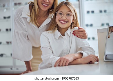 Close Up Portrait Of Happy Smiling Cute Teenager Girl In White Shirt With Adult Woman Sitting At The Desk In Optician Center