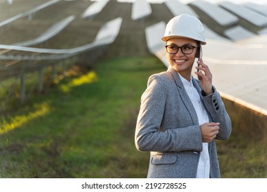 Close up portrait of happy smiling female in helmet talking on mobile phone while standing in front of the energy batteries in the countryside - Powered by Shutterstock