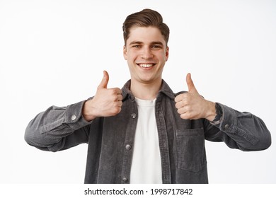 Close up portrait of happy smiling young man, boy shows thumbs up, nod approvingly, satisfied with choice, recommend something, praise or compliment, white background - Shutterstock ID 1998717842
