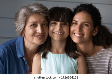 Close up portrait of happy three generations of Hispanic women, child, mom and grandma, pose together. Smiling Latino little girl kid with mother and grandmother show family unity and bonding.