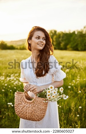close portrait of a happy woman looking at the camera in a light dress and a wicker basket in her hands with chamomile flowers in nature