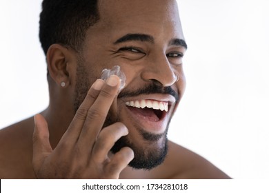 Close up portrait of happy young african American man apply moisturizing face cream for healthy glowing skin, smiling millennial biracial male use nourishing facial balm, skincare, hygiene concept