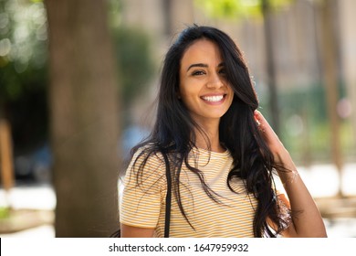Close up portrait of happy young arabic woman smiling with hand in hair outside