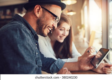 Close Up Portrait Of Happy Young Couple Using A Digital Tablet Together At A Coffee Shop. Young Man And Woman Looking At Touch Screen Computer And Smiling.