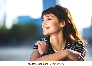 Close Up Portrait Of Happy Young Female Sitting Outside In The City Looking Away And Smiling