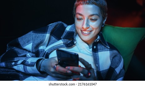 Close Up Portrait of a Happy Young Female with Short Hair Resting on a Couch at Home while Using a Smartphone. Beautiful Diverse Woman Browsing Web, Checking Social Media and Chatting with Friends. - Powered by Shutterstock