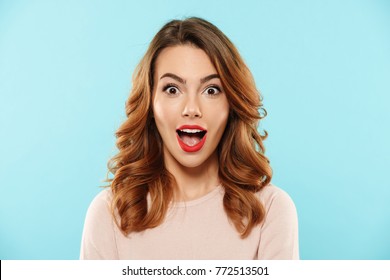 Close up portrait of a happy young girl dressed in sweater looking at camera with mouth open isolated over blue background