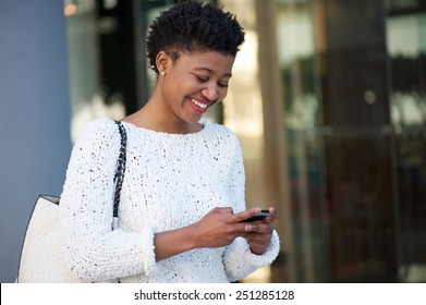 Close up portrait of a happy young woman walking in the city sending text message on cellphone