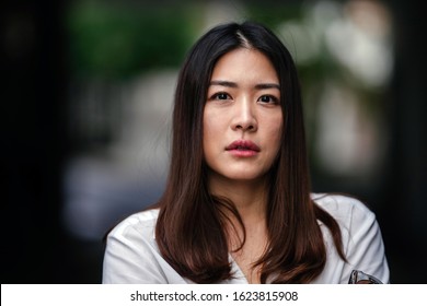 Close Up Portrait Head Shot Of The Face Of A Beautiful, Young And Attractive Thai Chinese Asian Woman In A Casual White Shirt Glaring Into The Camera. She Looks Serious, Concerned Or Worried.