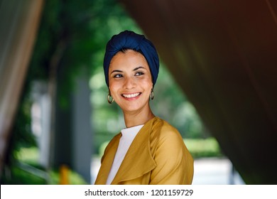 A Close Up Portrait Head Shot Of A Young And Attractive Malay Muslim Woman In A Turban (head Scarf, Hijab) In The City. She Is Smiling And Beaming Brightly. 