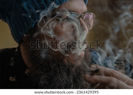 close up portrait of a hipster bearded man smoking a cigarette with a dense smoke in the air.