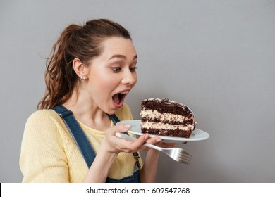Close Up Portrait Of A Hungry Young Pregnant Woman Going To Eat Chocolate Cake Isolated On A Gray Background