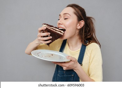 Close Up Portrait Of A Hungry Young Pregnant Woman Eating Chocolate Cake Isolated On A Gray Background