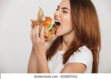 Close up portrait of a hungry young woman eating burger isolated over white background