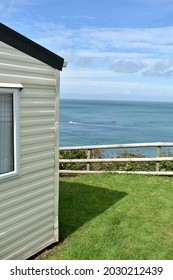 Close Up Portrait Image Of Mobile Home, Static Caravan, On Green Grass Cliff Edge With Ocean In Background On A Sunny Summers Day With Deep Blue Sky And White Clouds