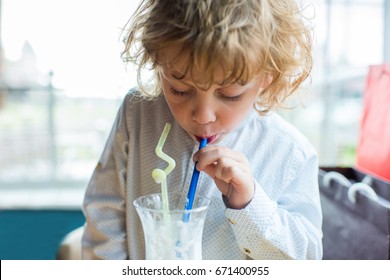 Close Up Portrait Of Kid Boy With Curly Hair Drinking Milkshake From Glass