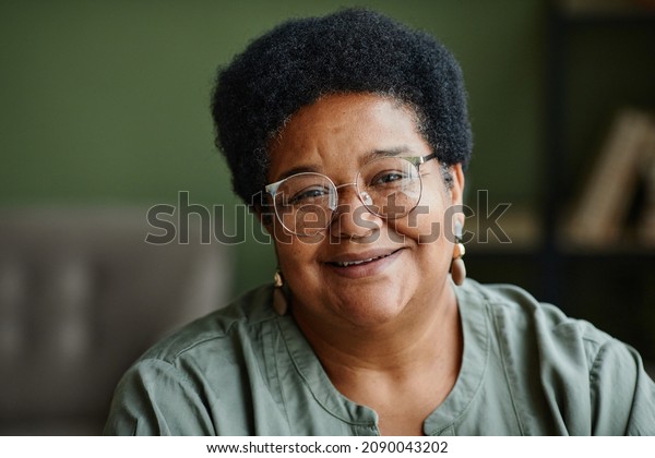 Close up portrait of kind black senior woman\
smiling at camera at home, copy\
space