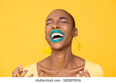 Close up portrait of laughing young African American woman with fashionable colorful make up isolated on yellow studio background - Shutterstock ID 1802870926