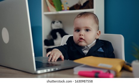 Close Up Portrait Of Little Adorable Baby Child In Business Suit In Home Office Looks Straight To Camera. Successful Confident Business Kid Smiling And Working On Laptop. Positive Emotions, Happiness.