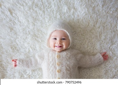 Close portrait of a little baby boy in white knitted onesie and a hat, smiling