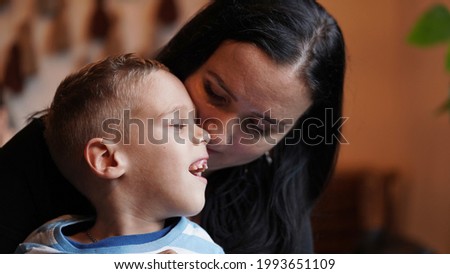 Close up portrait of a little boy with special needs and mom laughing at a table in a cafe, lifestyle. Mom's love for her child, inclusion.Happy disability kid concept.