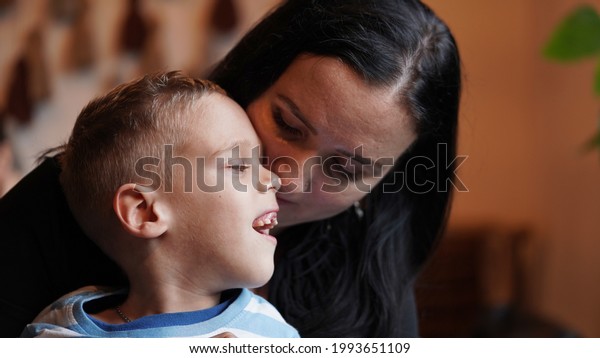 Close up portrait\
of a little boy with special needs and mom laughing at a table in a\
cafe, lifestyle. Mom\'s love for her child, inclusion.Happy\
disability kid concept.