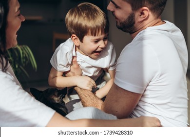 Close Up Portrait Of A Little Smiling Blond Boy. He Is Playing With Parents. Mother, Father Are Sharing Good Emotions While Relaxing At Home Natural Light, Terracotta Bed Linen. Happy Family.