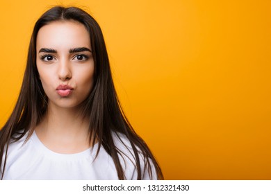 Close up portrait of a lovely european woman doing a kissing expression while looking into camera in front of yellow background.