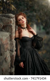 Close up portrait of magnificent Fashion gothic girl near stone wall .Fantasy art work.Amazing red haired model in black dress and hat looking at camera and posing.Fairytale about young princess 