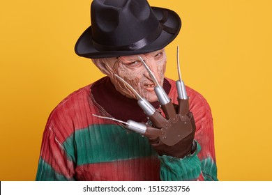 Close Up Portrait Of Male With Long Nose And Pointy Ears, Wearing Threadbare Sweater With Holes, Black Hat And Ugly Mask, Shows His Hand With Knives Instead Fingers To Camera, Looks Terrible And Nasty