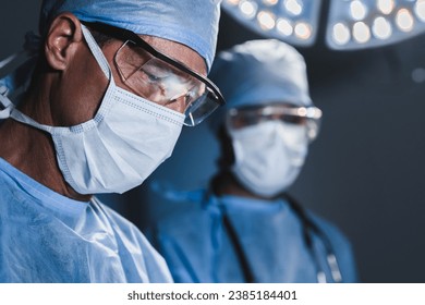 Close up portrait of male surgeon makes an operation. Concentrated doctor medical worker making decision during neurosurgery, looking at the patient in protective gown - Powered by Shutterstock