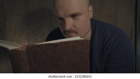 Close Up Of A Portrait Of Man Reading A Paper Book. He Is Sitting On Porch Of A Village House. The Concept Of Reading Paper Books, Studying And Hobbies. Dark Night. Old, Retro Decor Burlap Background