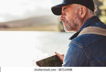 Close up portrait of mature man wearing cap sitting at a lake and looking at a view. Senior caucasian man with beard. - Powered by Shutterstock