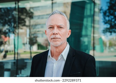 Close up portrait of a mature serious business man with aexecutive suit, gray hair, and successful attitude looking pensive at camera. Confident male welldressed corporate worker standing at workplace