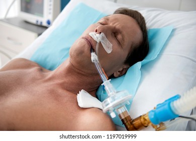 Close up portrait of middle aged man on breathing machine sleeping in hospital bed after surgery