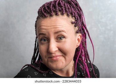 Close up portrait of middle-aged woman with pink dreadlocks writhing grimace. Emotion of surprise and smirk