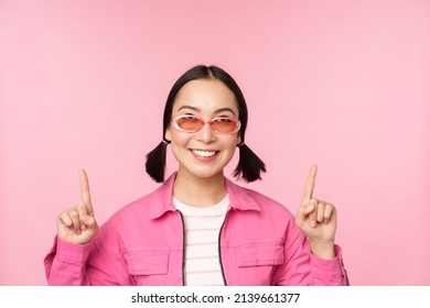 Close Up Portrait Of Modern Korean Female Model, Wears Sunglasses, Points Fingers Up, Shows Advertisement, Promo Banner, Pink Background