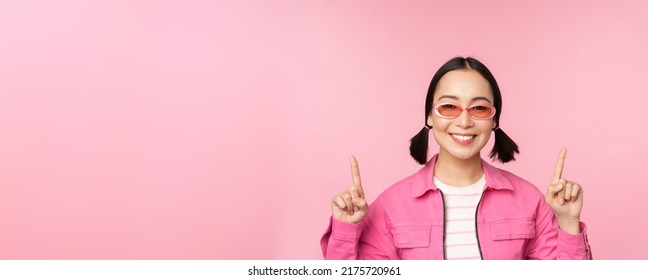 Close Up Portrait Of Modern Korean Female Model, Wears Sunglasses, Points Fingers Up, Shows Advertisement, Promo Banner, Pink Background