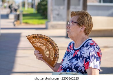 Close Portrait, Older Woman Fanning Herself On A Hot Day, Sitting On A Bench In The City.