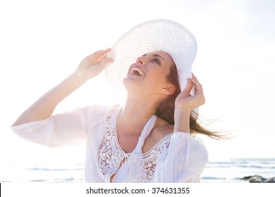 Close Up Portrait Of An Older Woman Laughing With Hat At The Beach