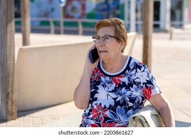 Close Portrait, Older Woman Talking On The Phone Sitting On A Bench In The City