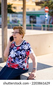 Close Portrait, Older Woman Talking On The Phone Sitting On A Bench In The City