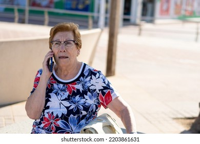 Close Portrait, Older Woman Talking On The Phone Sitting On A Bench In The City