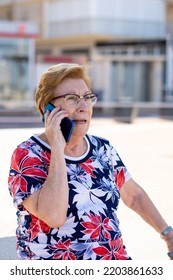 Close Portrait, Older Woman Talking On The Phone Sitting On A Bench In The City