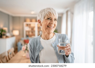 Close up portrait of one senior woman with short hair happy smile positive emotion copy space standing at home indoor gray white hair hold glass of water - Powered by Shutterstock