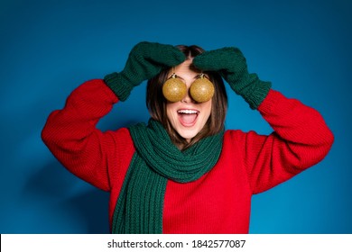 Close up portrait photo of cute playful young girl open mouth hold two baubles hiding eyes funny decorating house wear red pullover green scarf gloves isolated dark blue color background