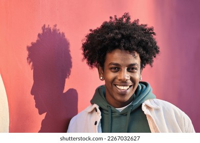 Close up portrait photo of young stylish happy African American cool hipster guy face laughing on red city wall lit with sunlight. Smiling cheerful cool gen z male model standing outdoors. Headshot.