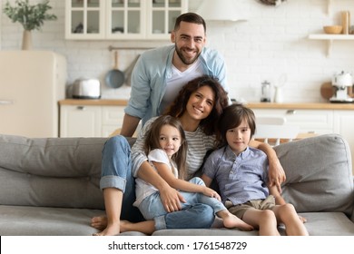 Close up portrait picture of happy young family of four people sitting on couch at home. Smiling parents with little children hugging looking at camera posing for photo in living room. - Shutterstock ID 1761548729